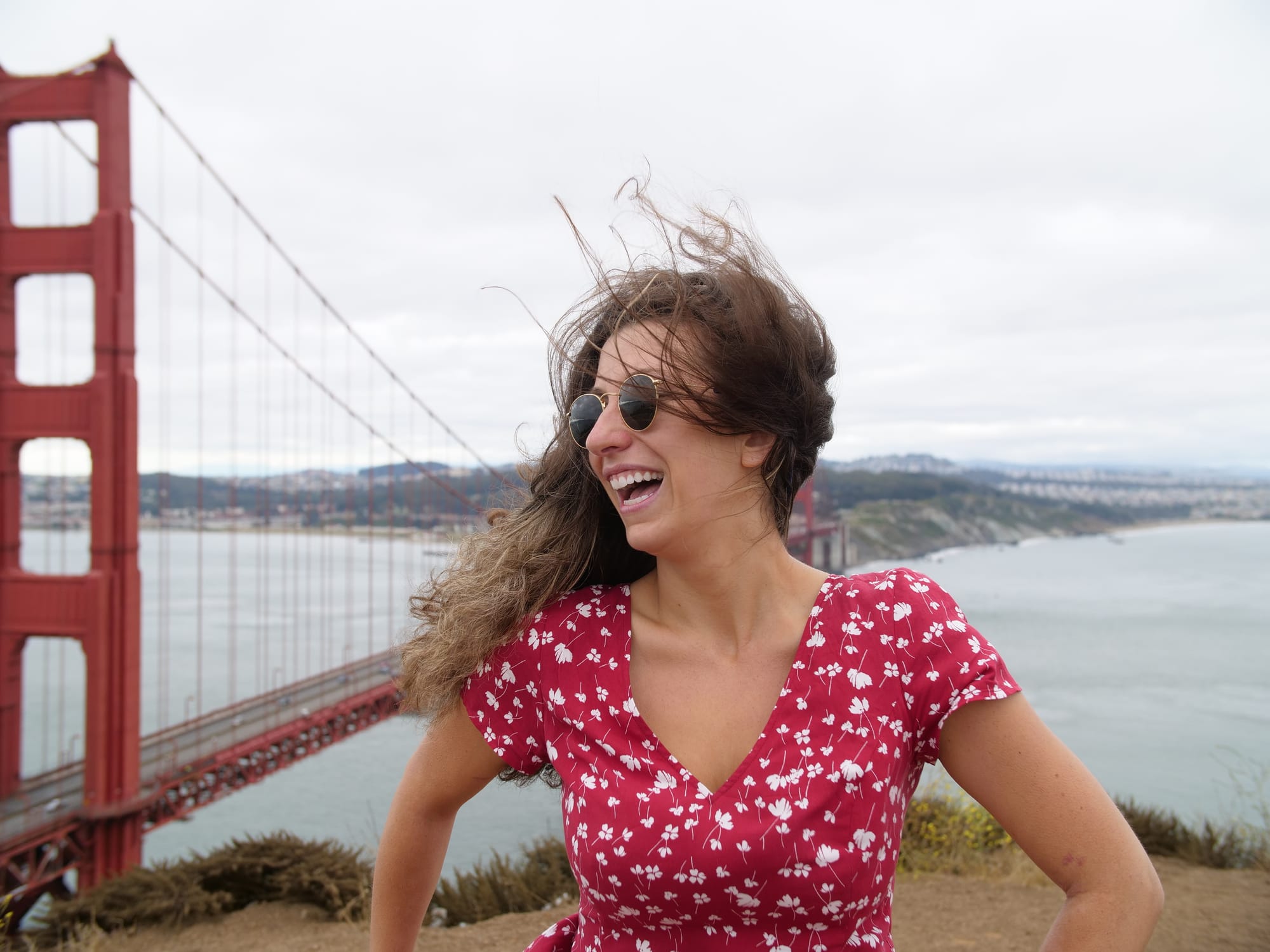 Woman smiles and laughs while posing for a photo in front of the Golden Gate Bridge in San Francisco. 