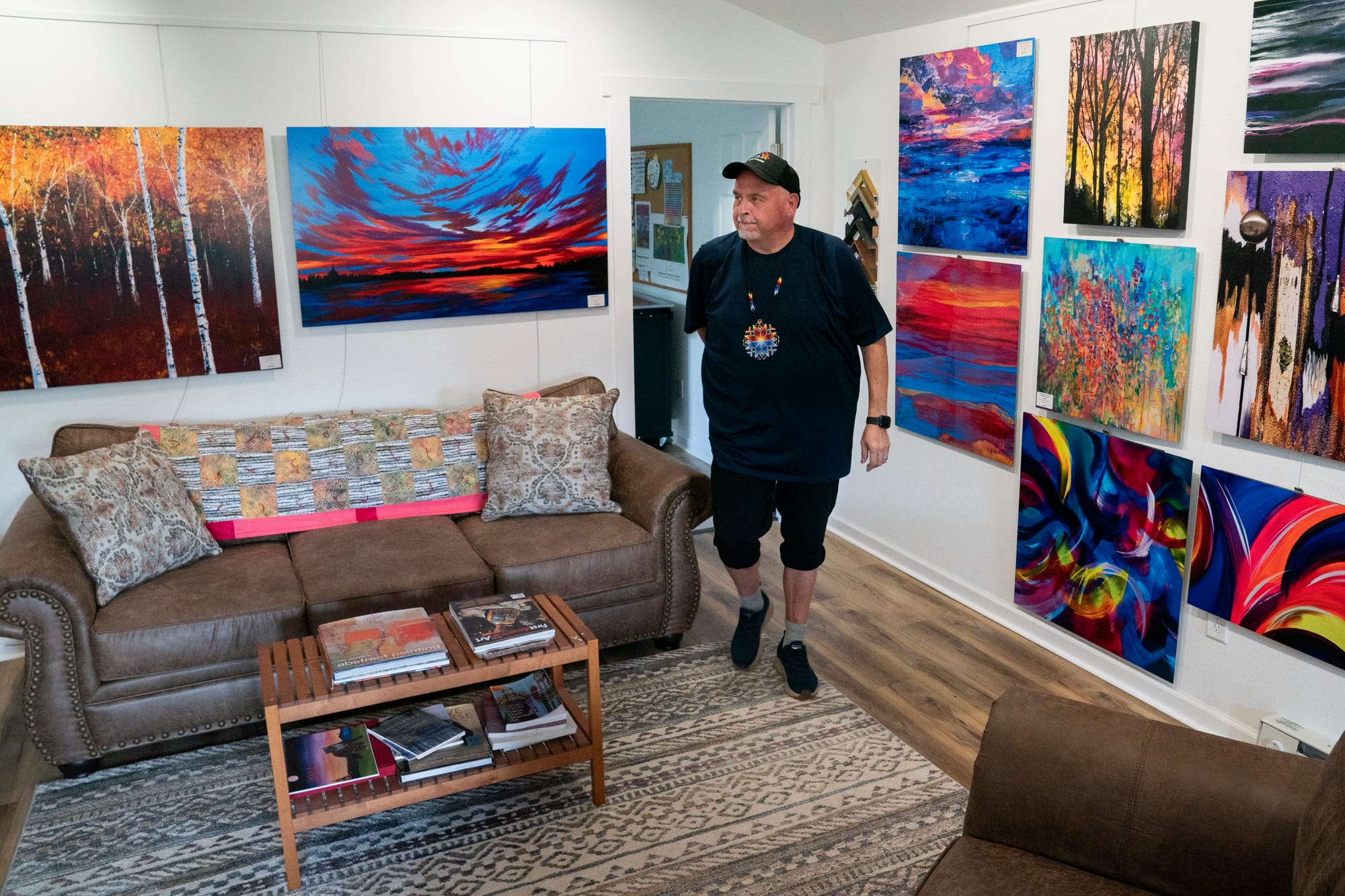 Man walks through his studio. The walls are covered with brightly-colored paintings. 