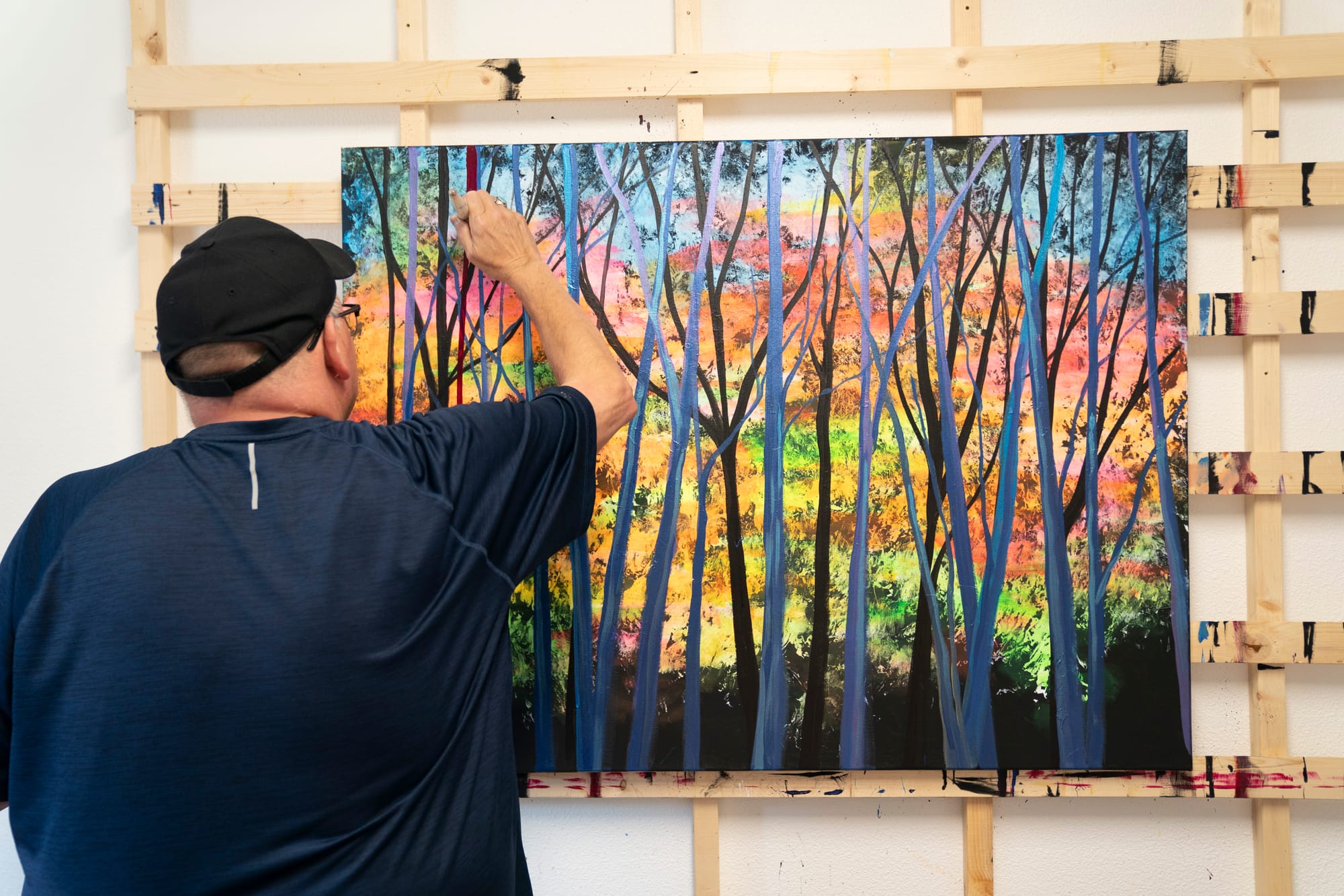 Man stands in front of a painting, adding to it. 