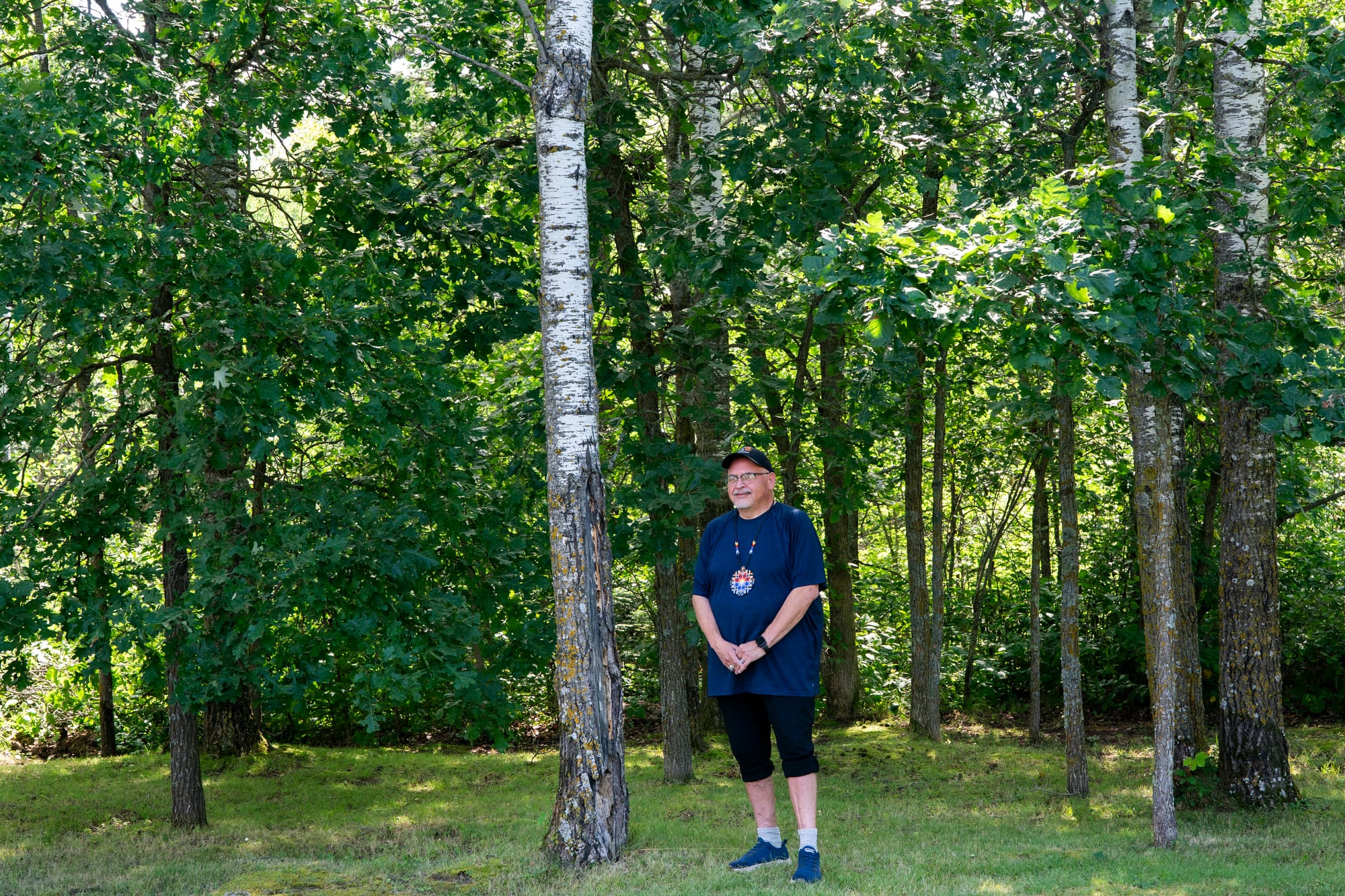 Man stand with his hands clasped in front of him by trees on his property. 