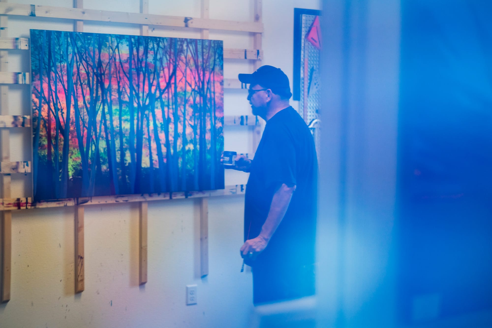 Man is reflected in one of his paintings as he stands looking at another painting. 