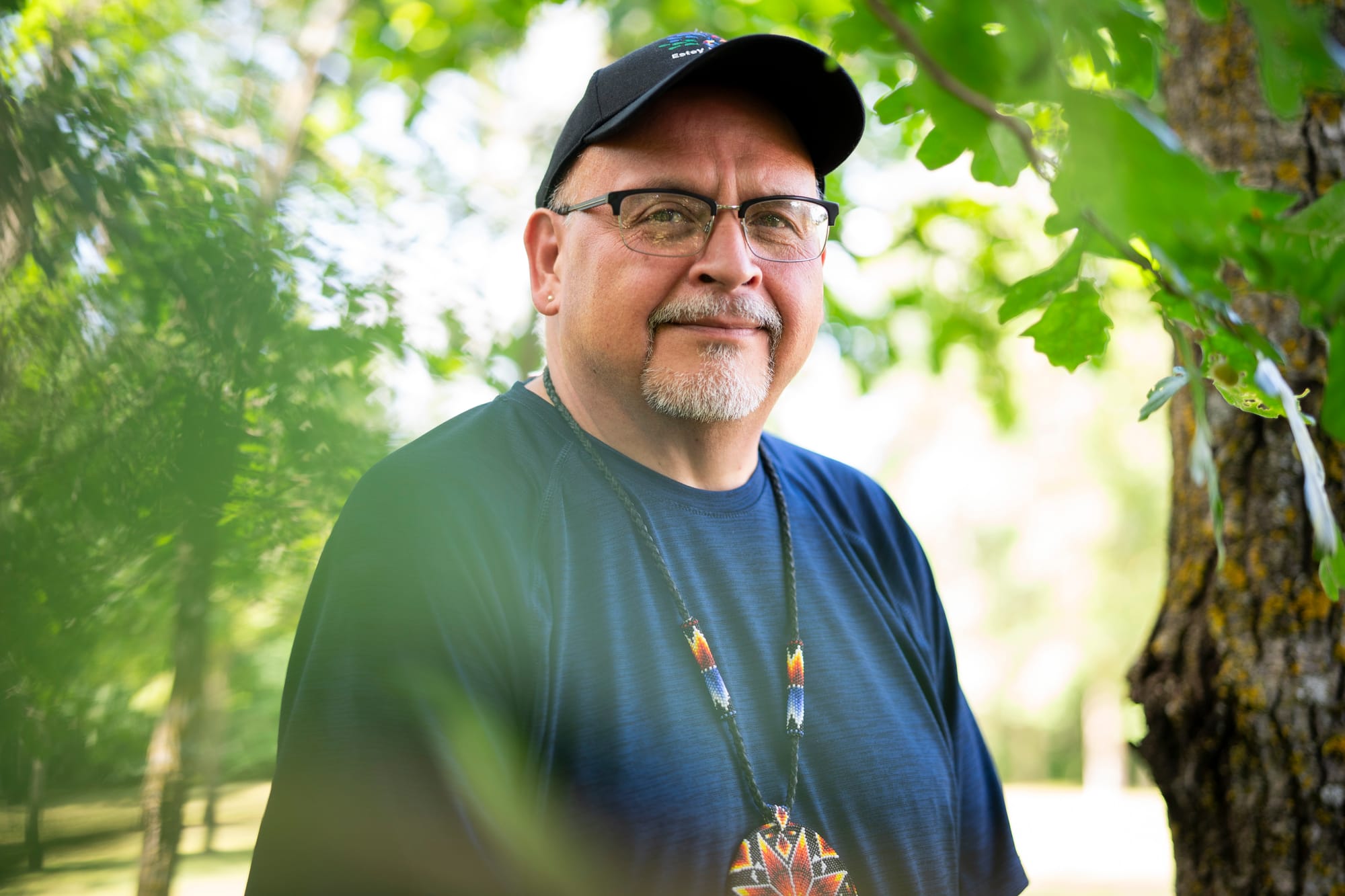 Man poses for a portrait next to trees with the sun shining. 