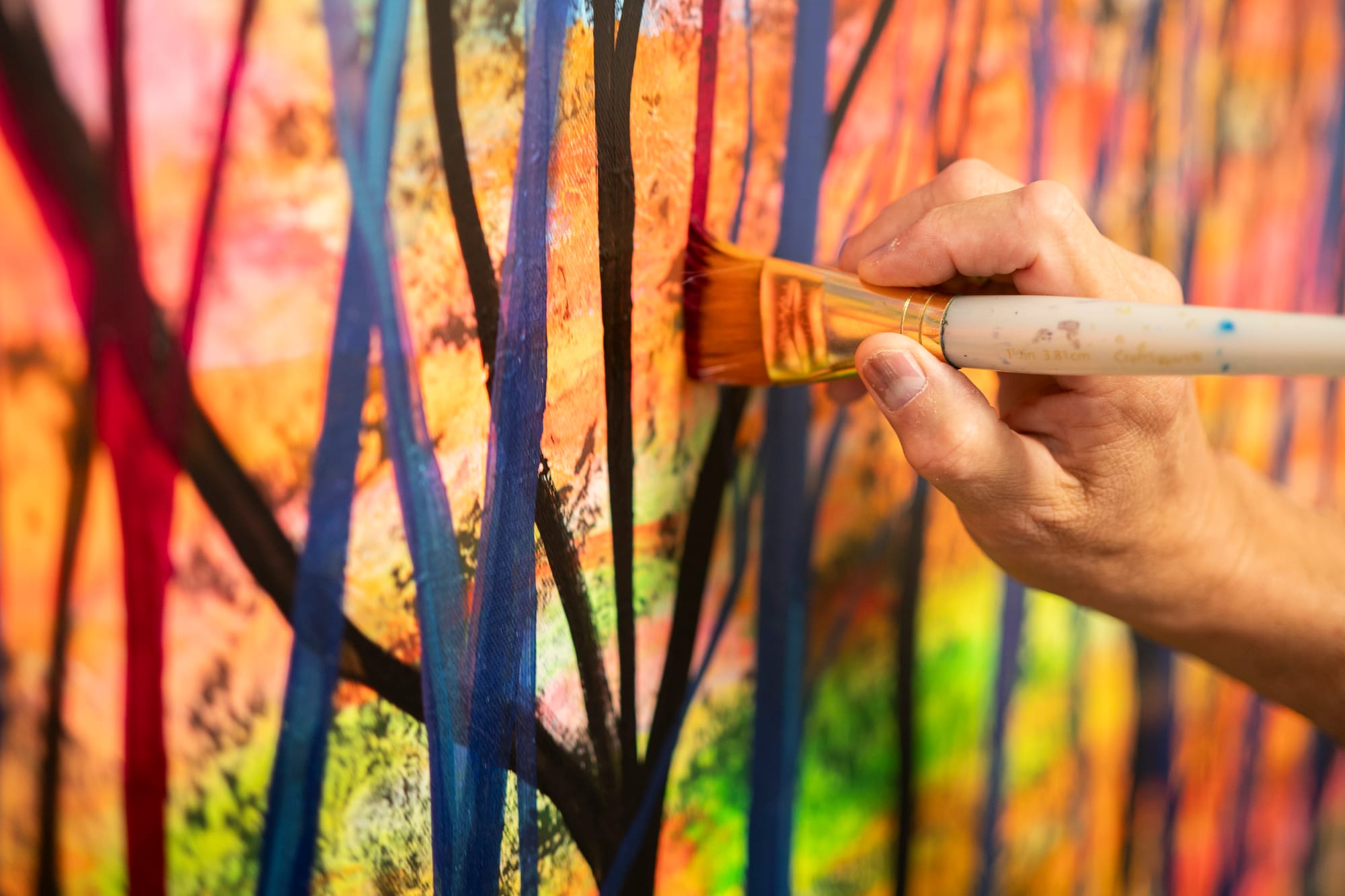 A close up photo of a man's hand holding a paintbrush, adding paint to a canvas. 