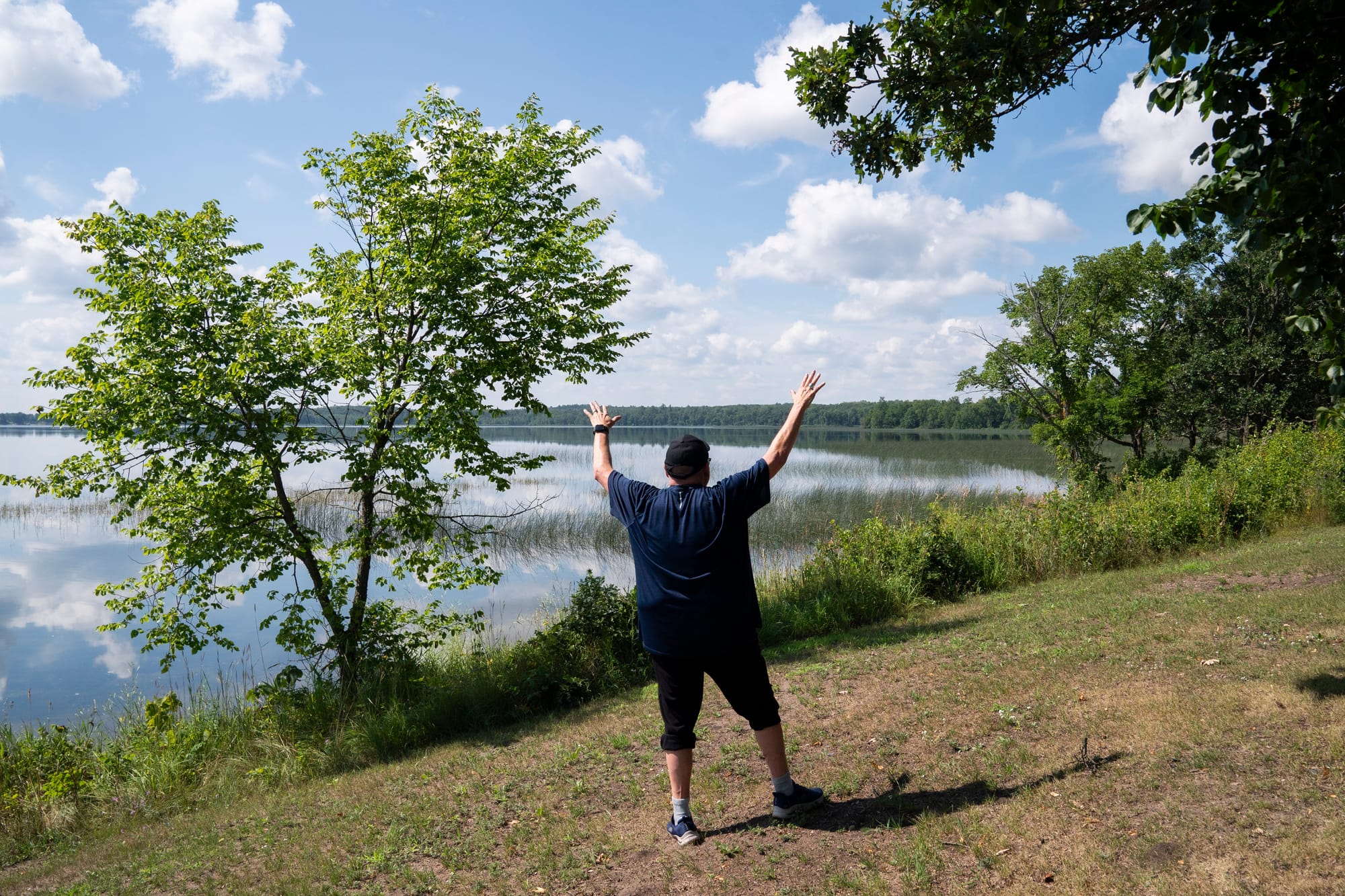 Man stands on a hill gesturing toward the nearby lake that inspires his artwork. 