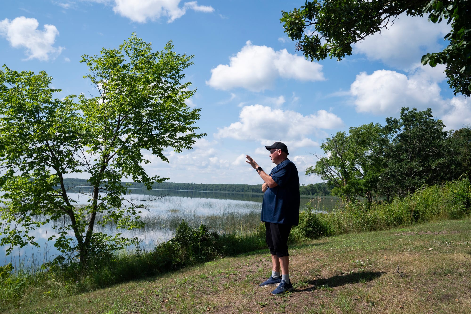 Man stands on a small hill overlooking a lake on a clear, sunny summer day. 