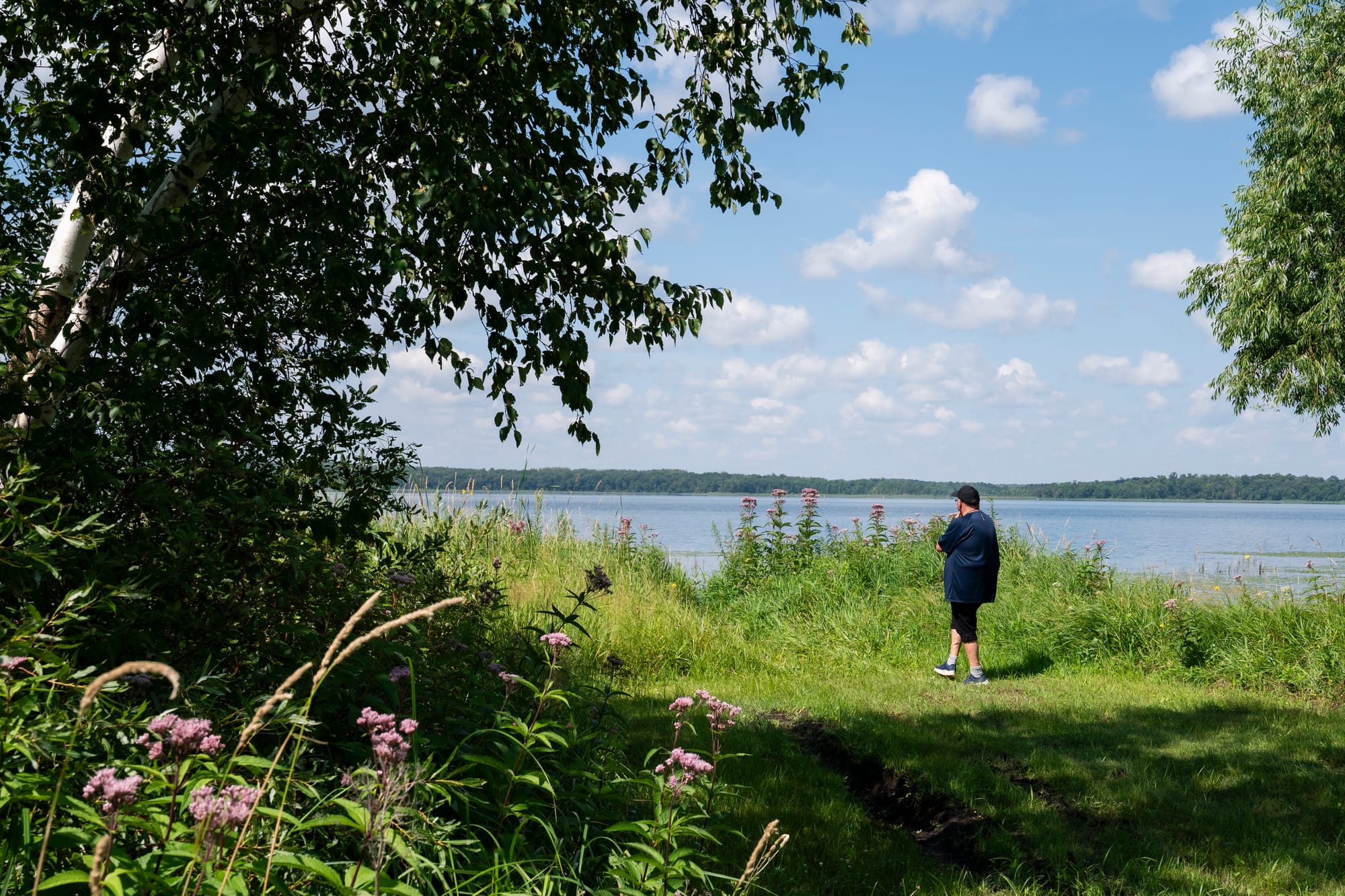 A man stands on the shore looking out a the lake. 