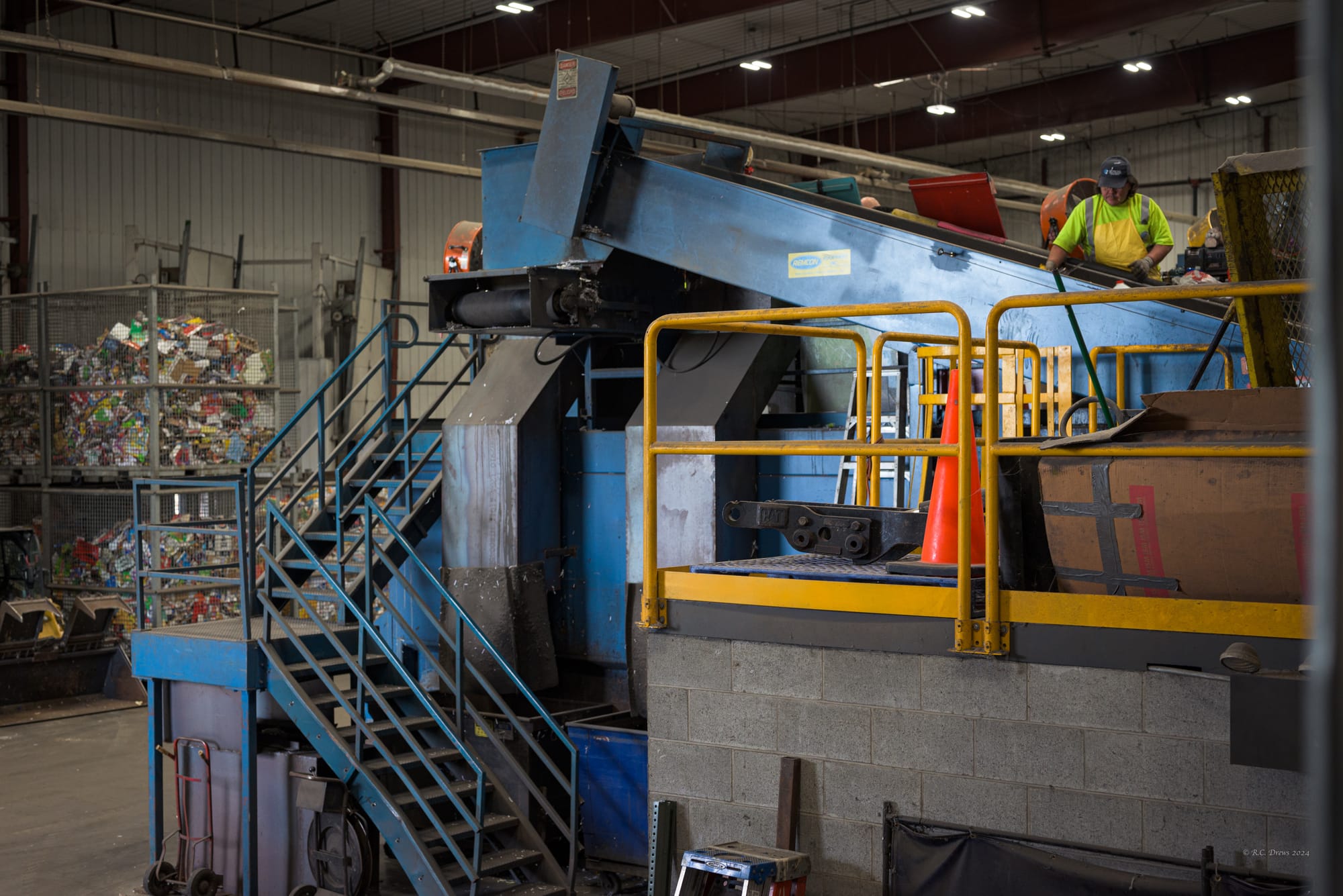 A worker stands next to a conveyor belt sorting plastics. 