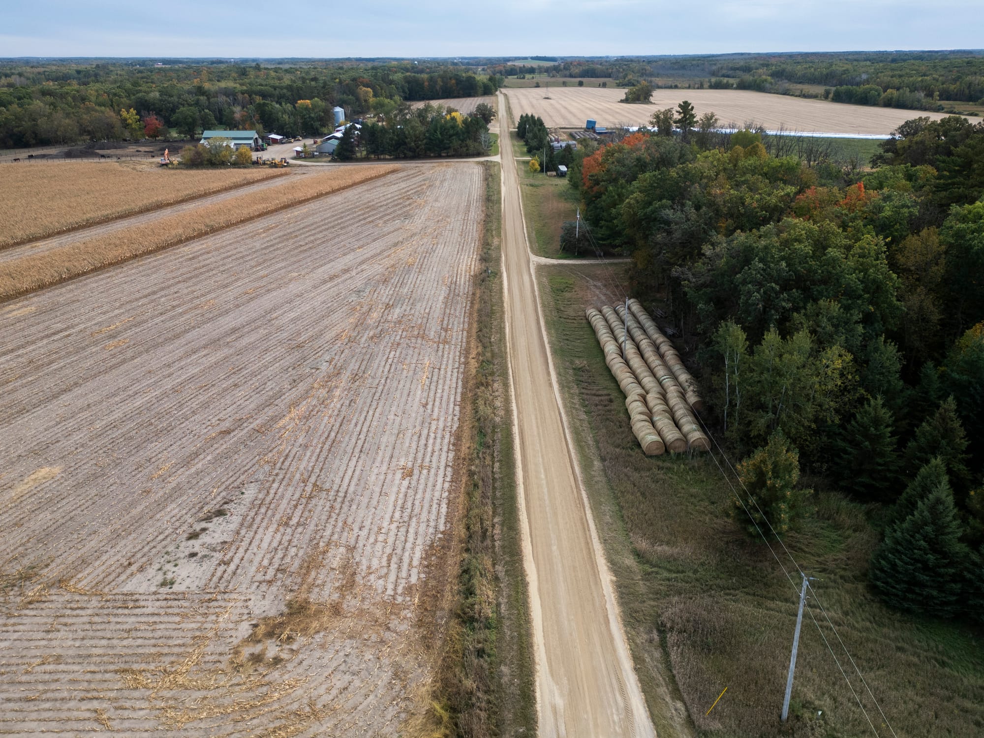 An aerial view of empty fields next to a woods with a few leaves changing.