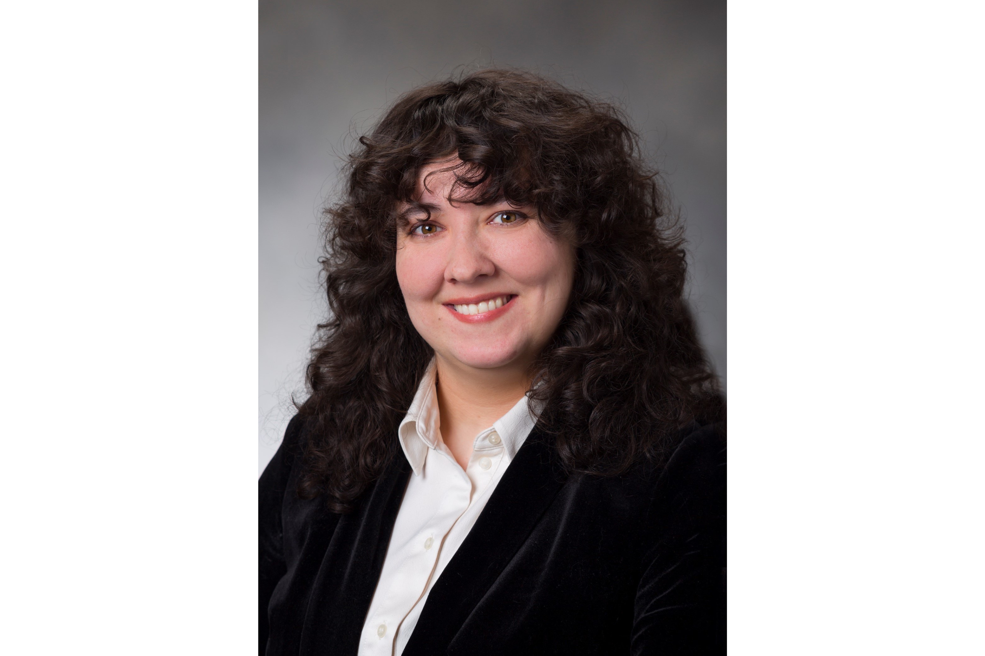 Woman with dark, curly hair poses for a professional portrait. 