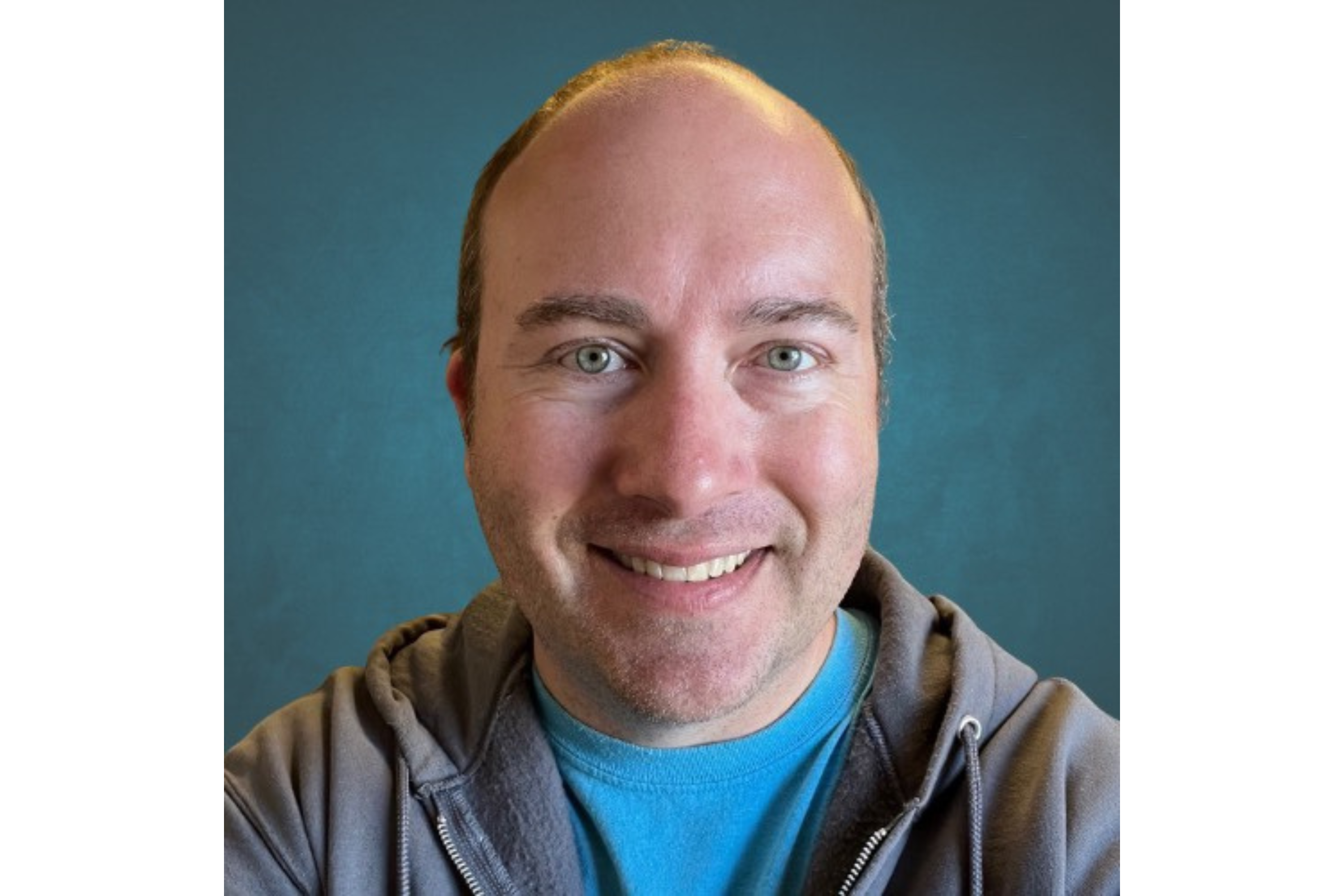 Man wearing a T-shirt and hoodie smiles for a selfie. 