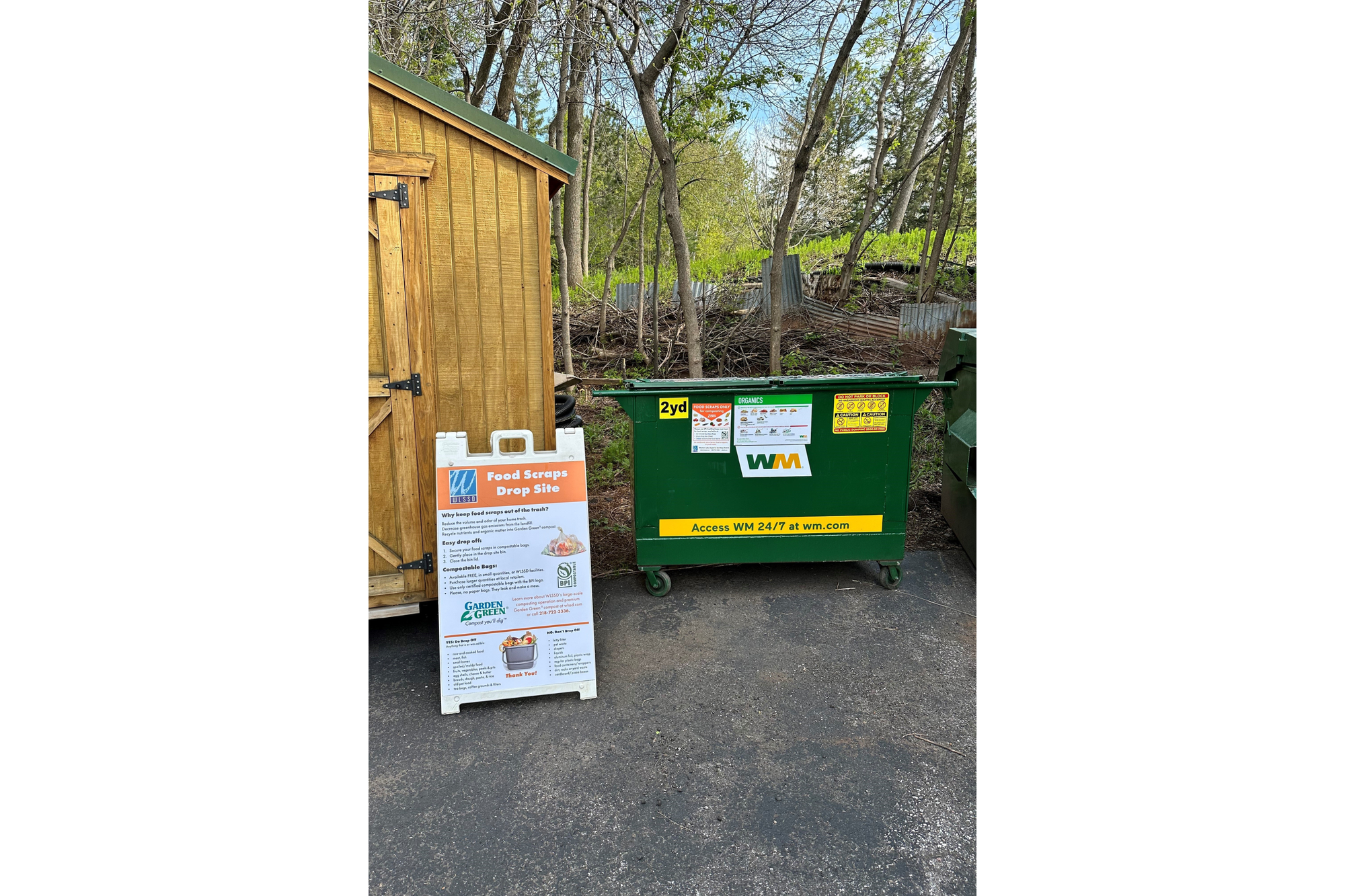 A food waste dumpster sits next to a shed.