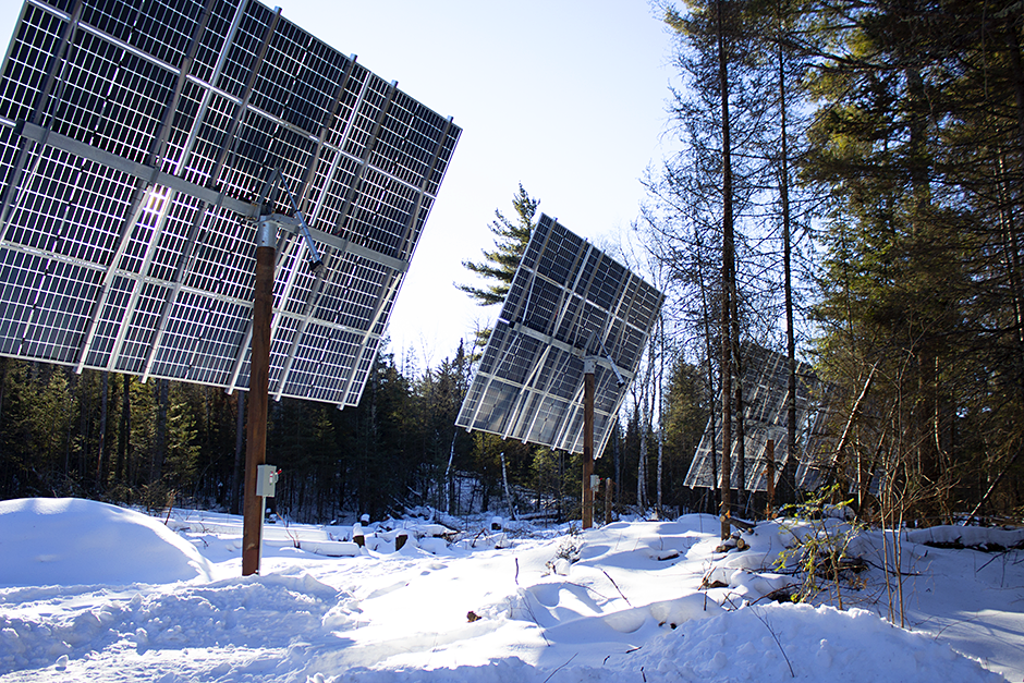 A large solar array is seen in a snowy, wooded landscape. 