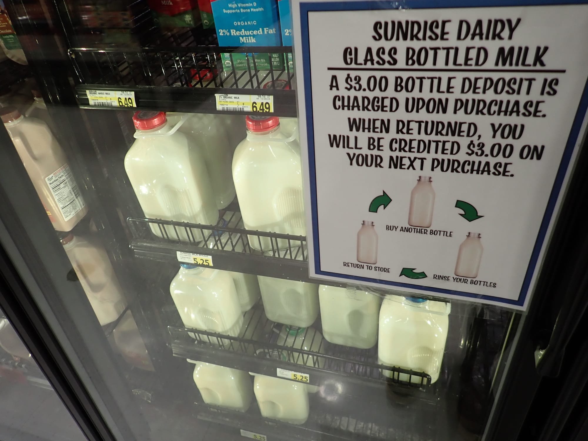 Glass milk bottles are pictured in a grocery store cooler. 