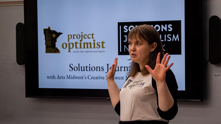 Woman stands in front of a powerpoint projector while giving a presentation on solutions journalism.