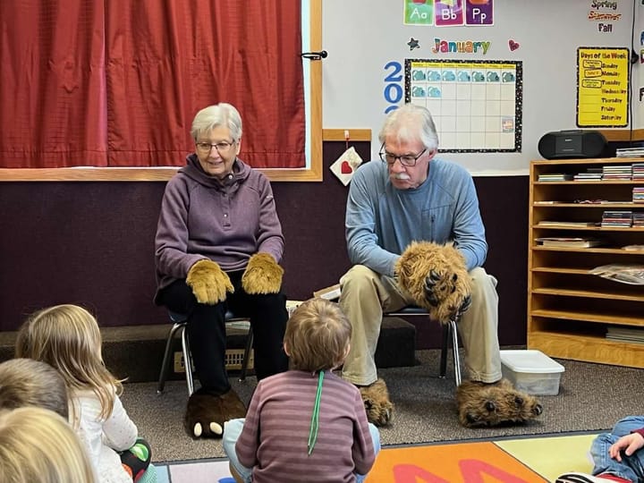 Woman and man wear fuzzy gloves and slippers during nature lesson for kids. 