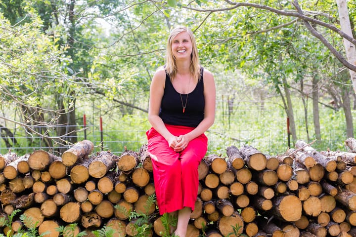 Woman sits on a woodpile while posing for a photo.