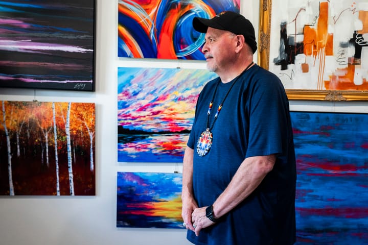 Man poses for a portrait in front of his paintings. 