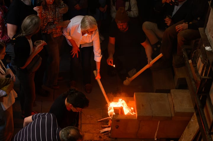 A woman uses a handmade torch to light a kiln. 