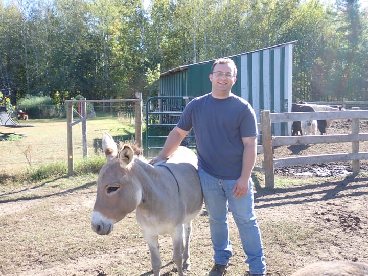 Man stands next to donkey in a pasture on his farm. 