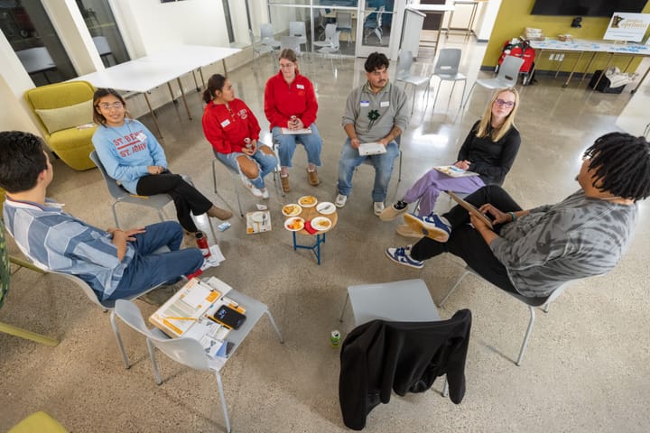 Students sit in a half-circle during an event and share their experiences. 